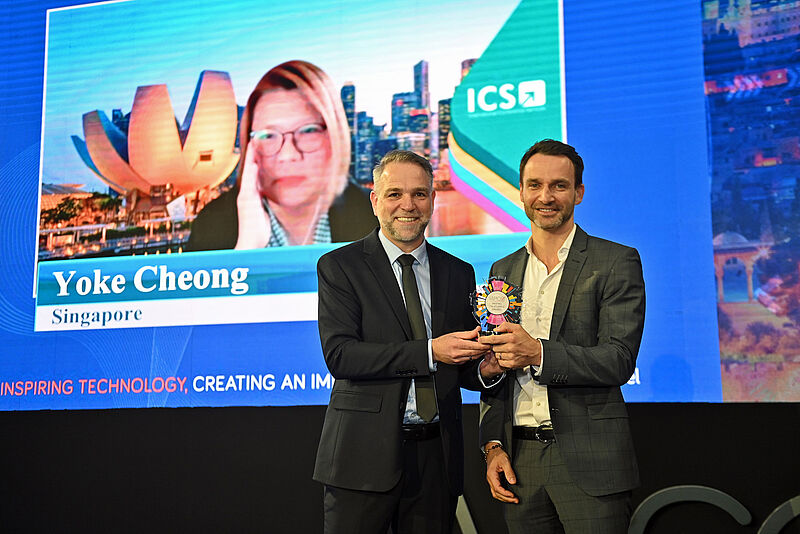 Yoke Cheong of ICS joined online live on the big screen as ICS Chairman and Partner Mathias Posch received the award on her behalf from IAPCO President Ori Lahav. Photo: IAPCO