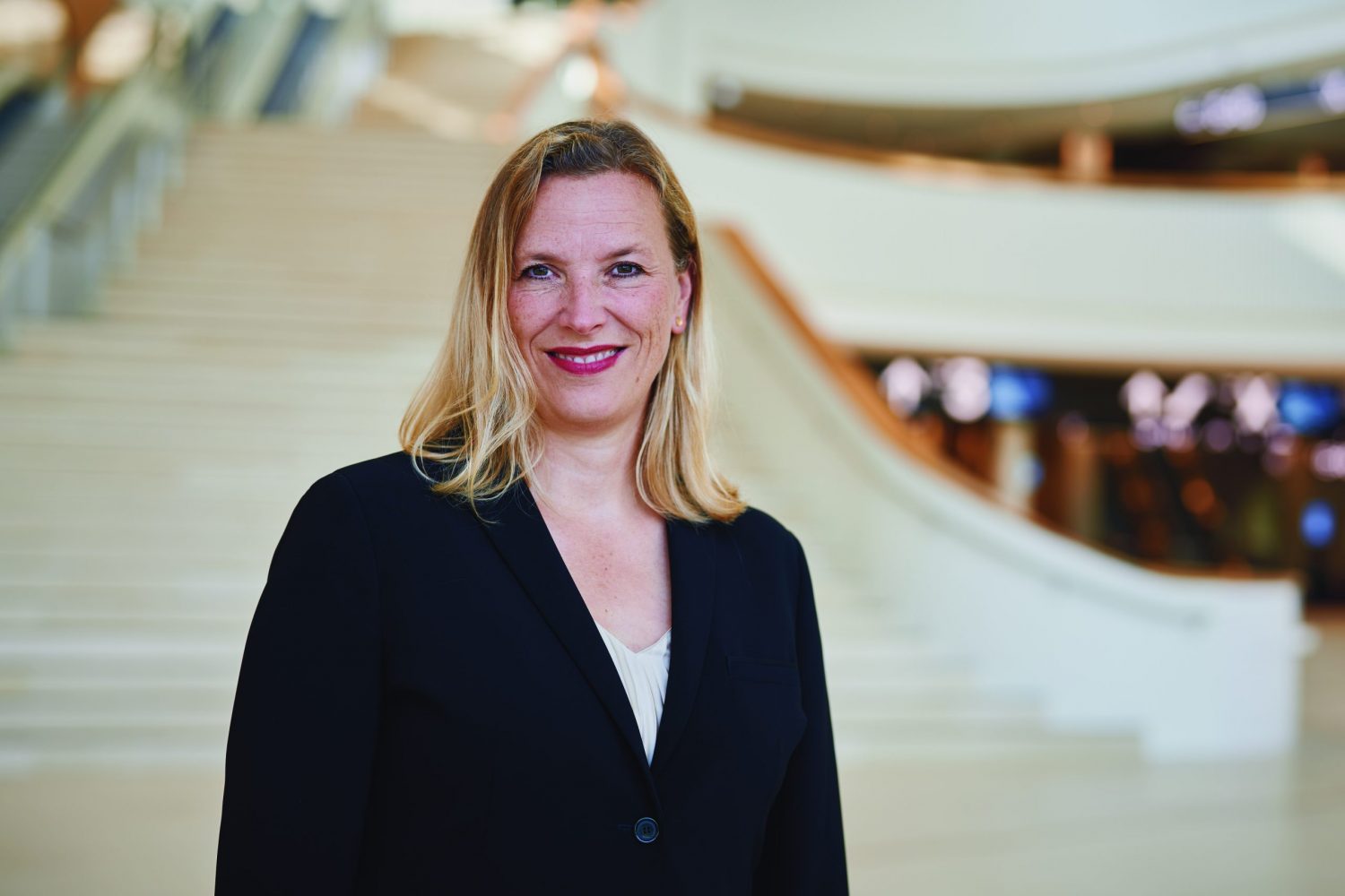 Blonde Frau steht vor heller Treppe