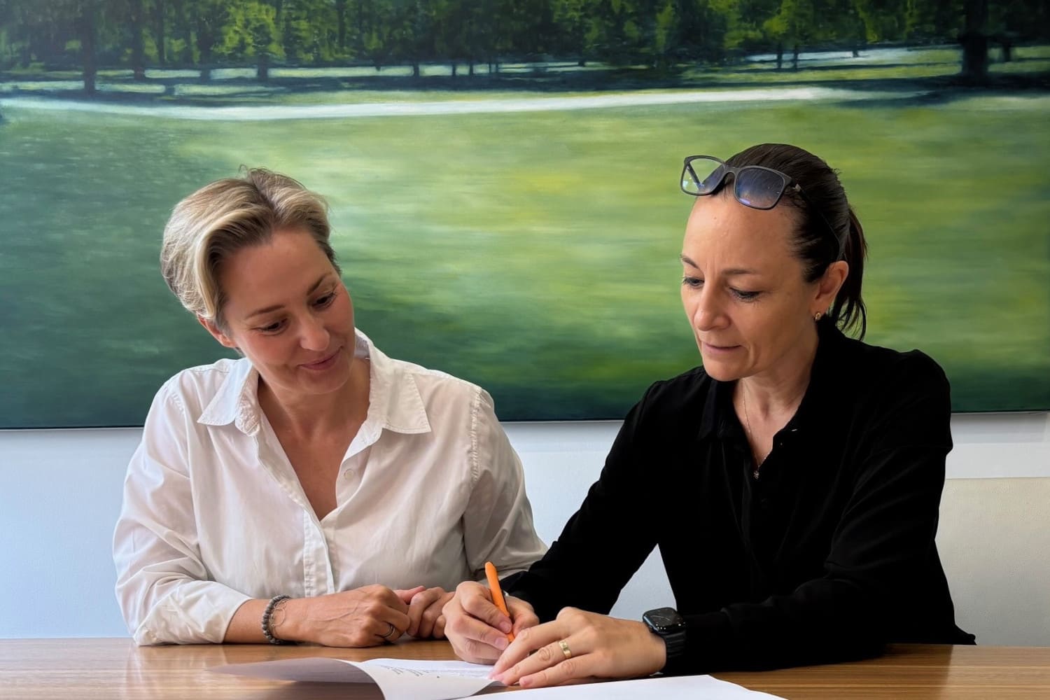 2 Frauen sitzen am Tisch und unterzeichnen ein Dokument