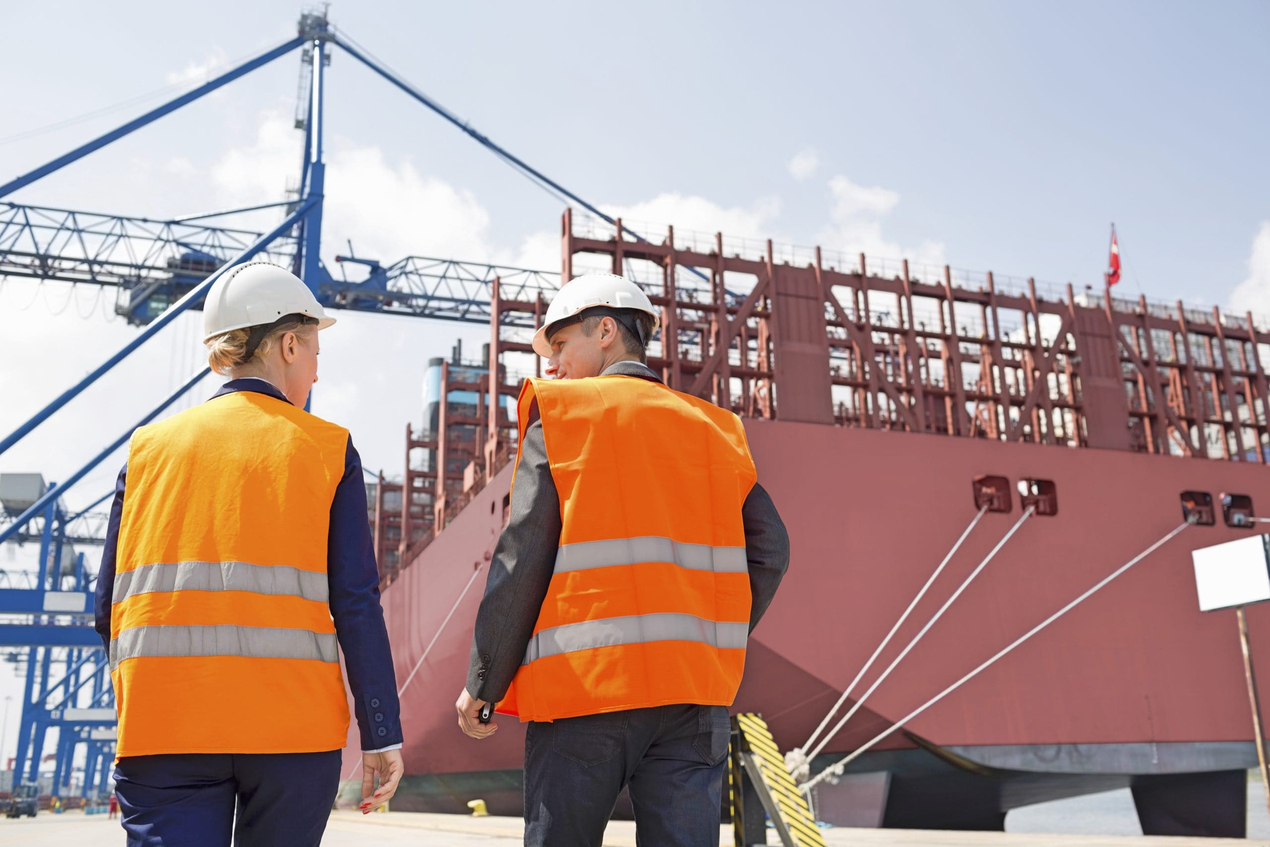 Mann und Frau mit orangenen Warnwesten in einem modernen Hafen