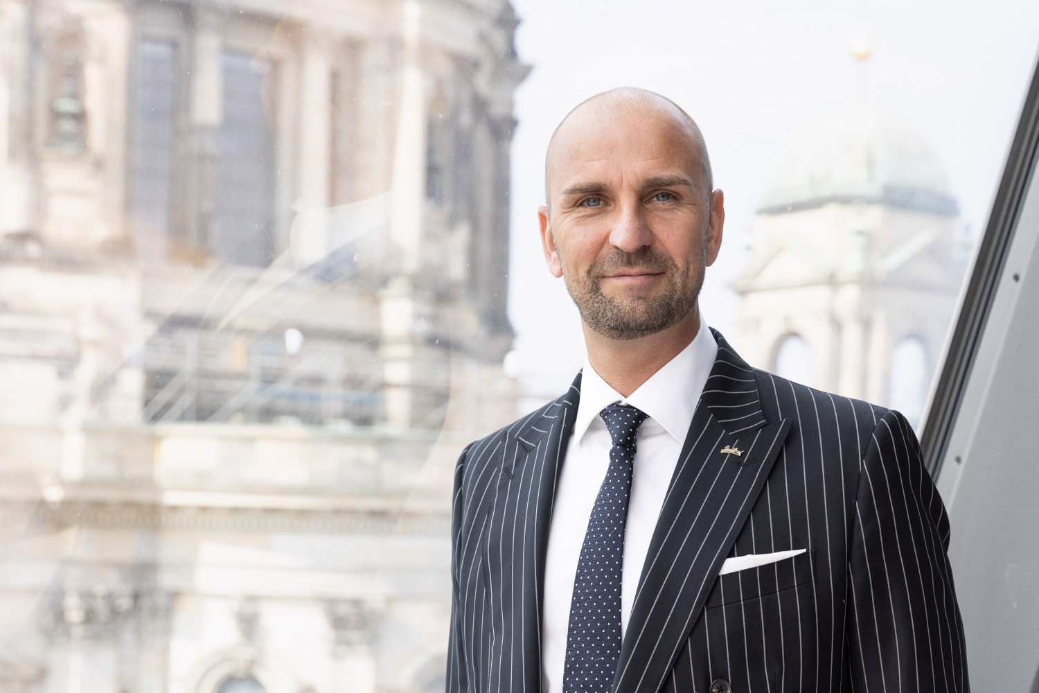 Mann in Anzug vor Fenster, historisches Gebäude im Hintergrund
