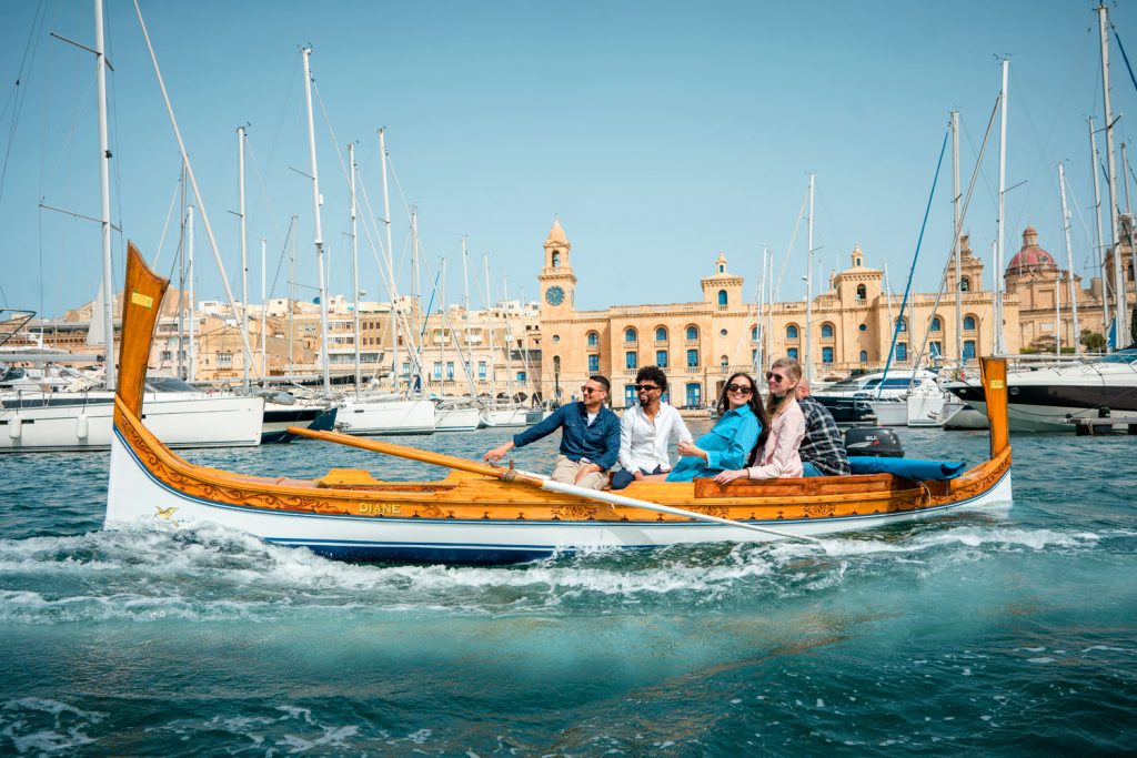 Fröhliche Menschen im traditionellen Holzboot vor der Kulisse Vallettas