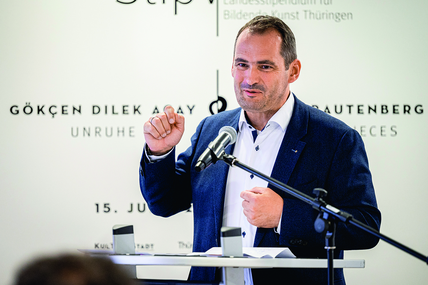 Mann steht vor Mikrophon, trägt blauen Anzug