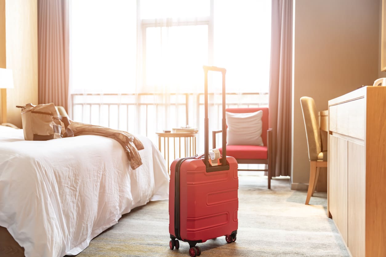 Hotelzimmer mit großem Schlafsofa und rotem Koffer, Gast gerade eingecheckt