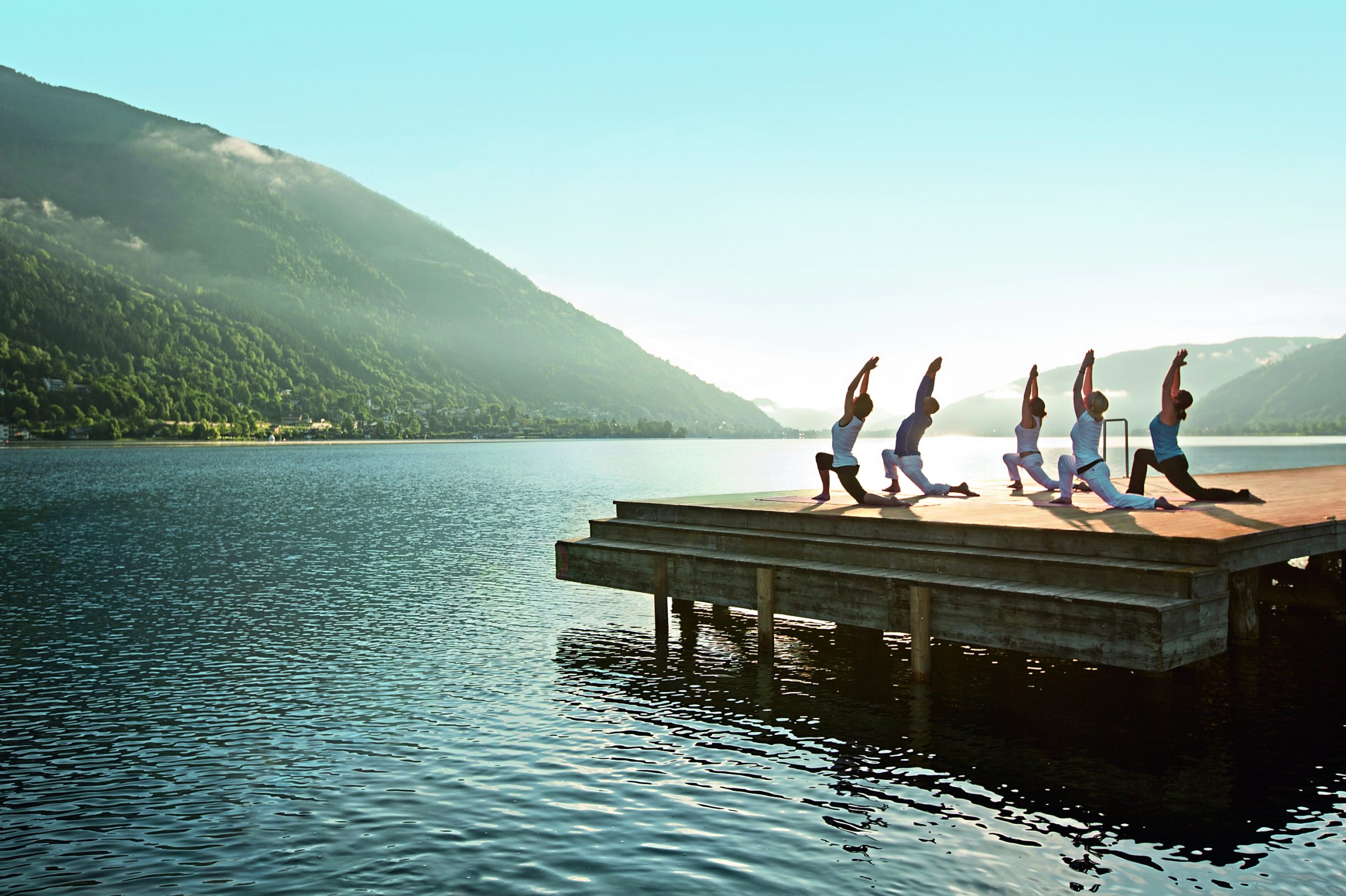 Personen machen Yoga auf Steg an See