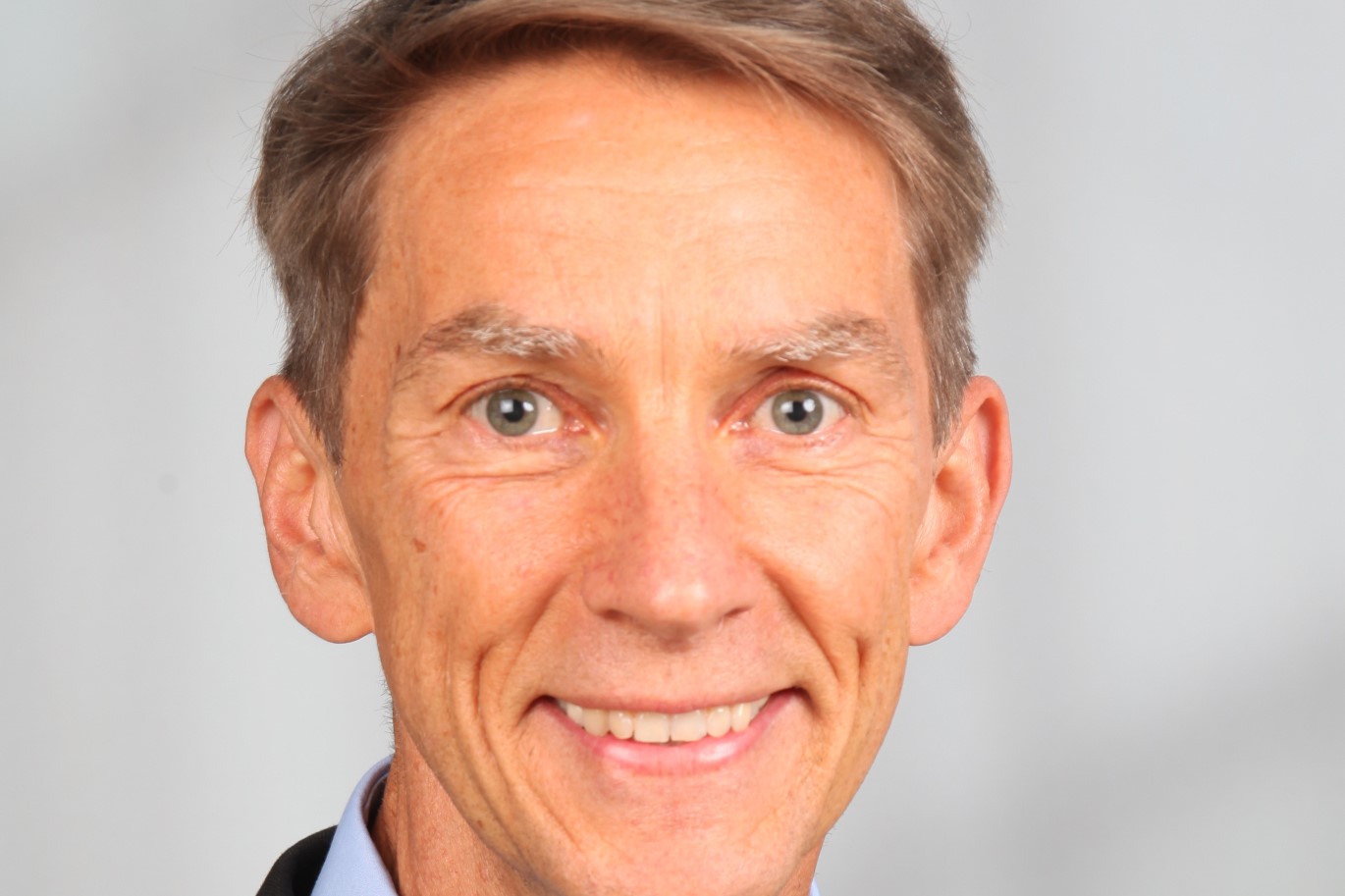 Mann lächelt in die Kamera, hellgrauer Hintergrund
