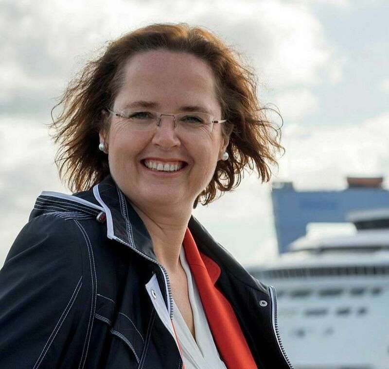 Frau lächelt in Kamera, im Hintergrund Schiff und grauer Himmel zu sehen