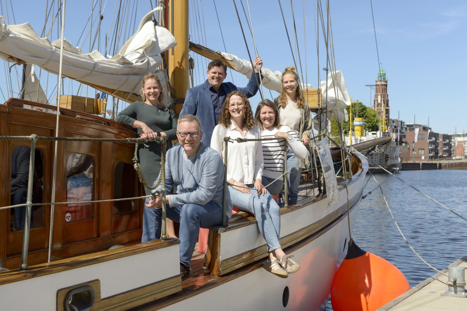 Männer und Frauen sitzen auf einem Segelboot in der Sonn eund lächeln in die Kamera