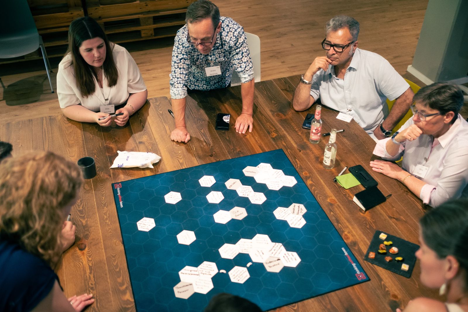 Erwahsene Menschen sitzen um einen Holztisch und spielen eine Art Brettspiel